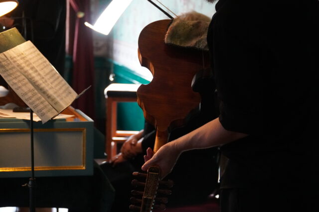 A person in black holds a musical instrument in front of a music stand.