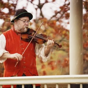 man in red vest playing a fiddle with fall leaves in background